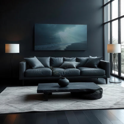A moody, modern living room with dark walls and a large canvas reading &quot;All Storms Pass&quot; above a black leather sofa. The space includes soft gray cushions, black coffee table, light gray rug, and two tall lamps, with natural light streaming in.