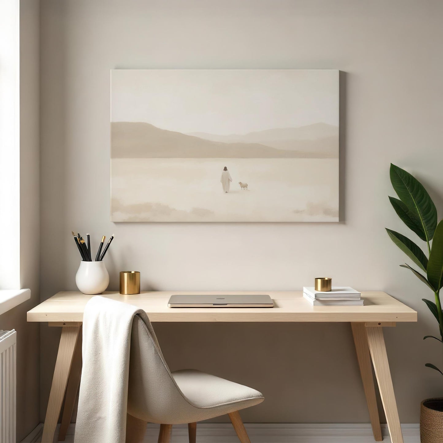 A cozy workspace with a light wood desk, beige chair, and minimalist decor, including a laptop, gold accents, and a plant. Above the desk hangs a serene gallery-wrapped canvas of Jesus and a lost sheep in a soft desert landscape.
