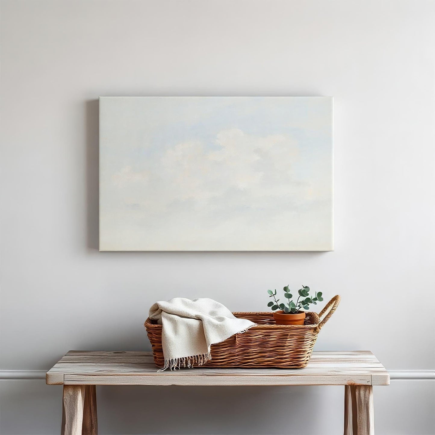 Soft cloudscape canvas above a rustic wooden console. Styled with a woven basket, cozy throw, and potted greenery for a serene, minimalist home decor aesthetic.