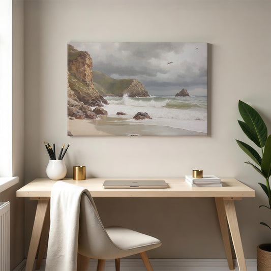 A beach canvas print showcasing waves rolling onto the shore, dramatic cliffs, and a moody sky with seagulls. The artwork is styled above a wooden desk with neutral decor, creating a calming workspace atmosphere.