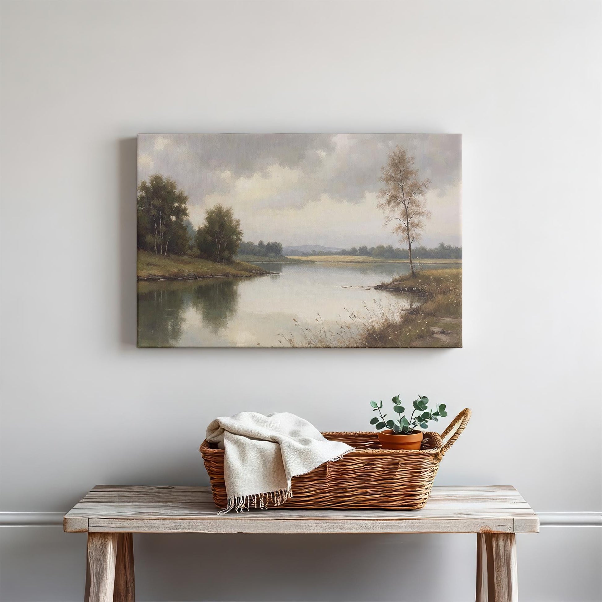 A cozy home interior setting featuring the framed lake landscape canvas above a minimalist wooden console table. The decor includes neutral-colored accents like a woven basket, candles, and soft textiles.
