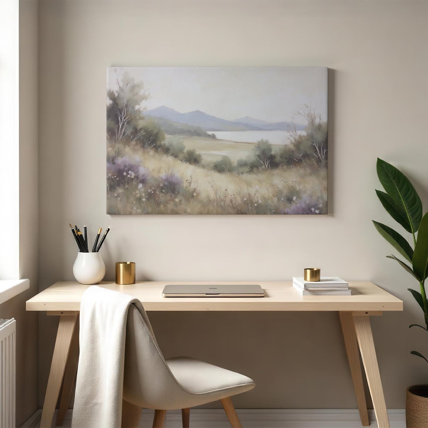 A cozy home office with a light wood desk, cushioned chair, and elegant decor. A landscape canvas of rolling hills, a still lake, and wildflowers hangs above, bringing a peaceful, nature-inspired ambiance to the workspace.