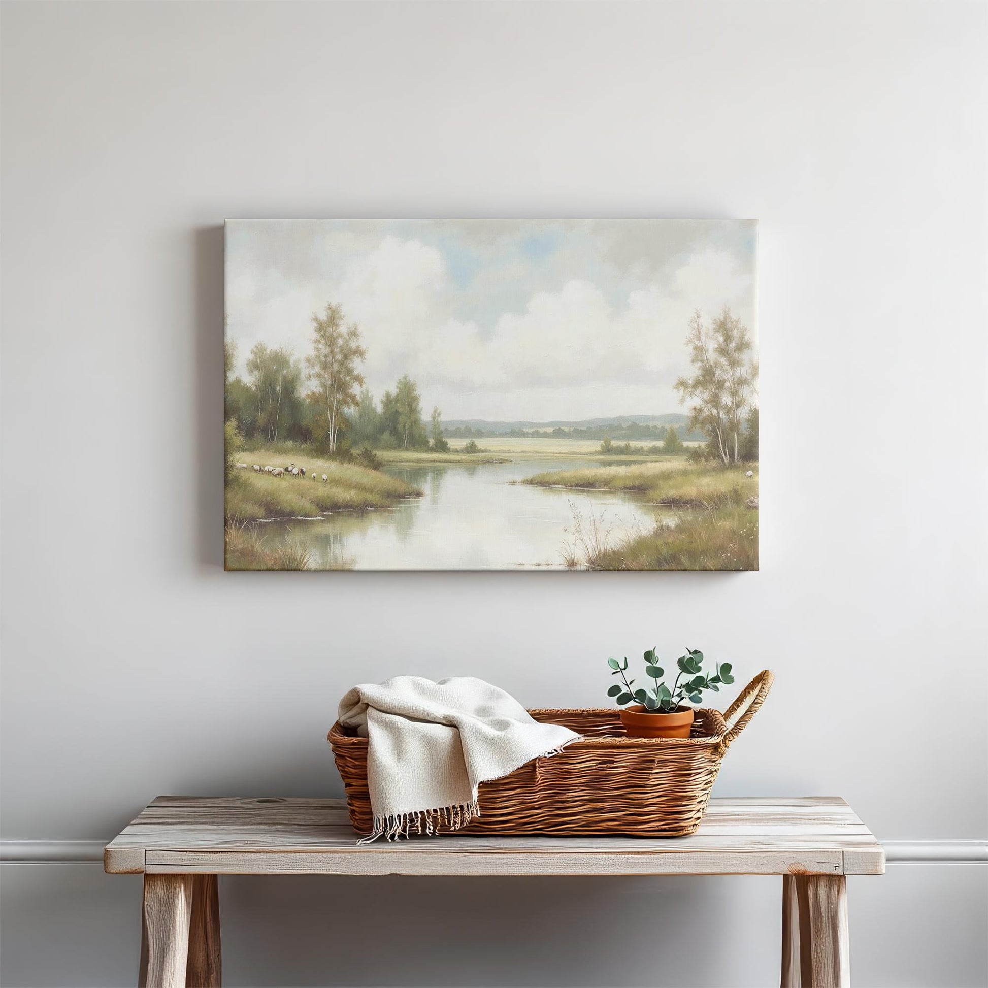 A rustic console table with a woven basket, a folded white blanket, and a potted plant sits beneath a landscape canvas of a river with trees. The neutral decor and soft colors create a calming and inviting aesthetic.