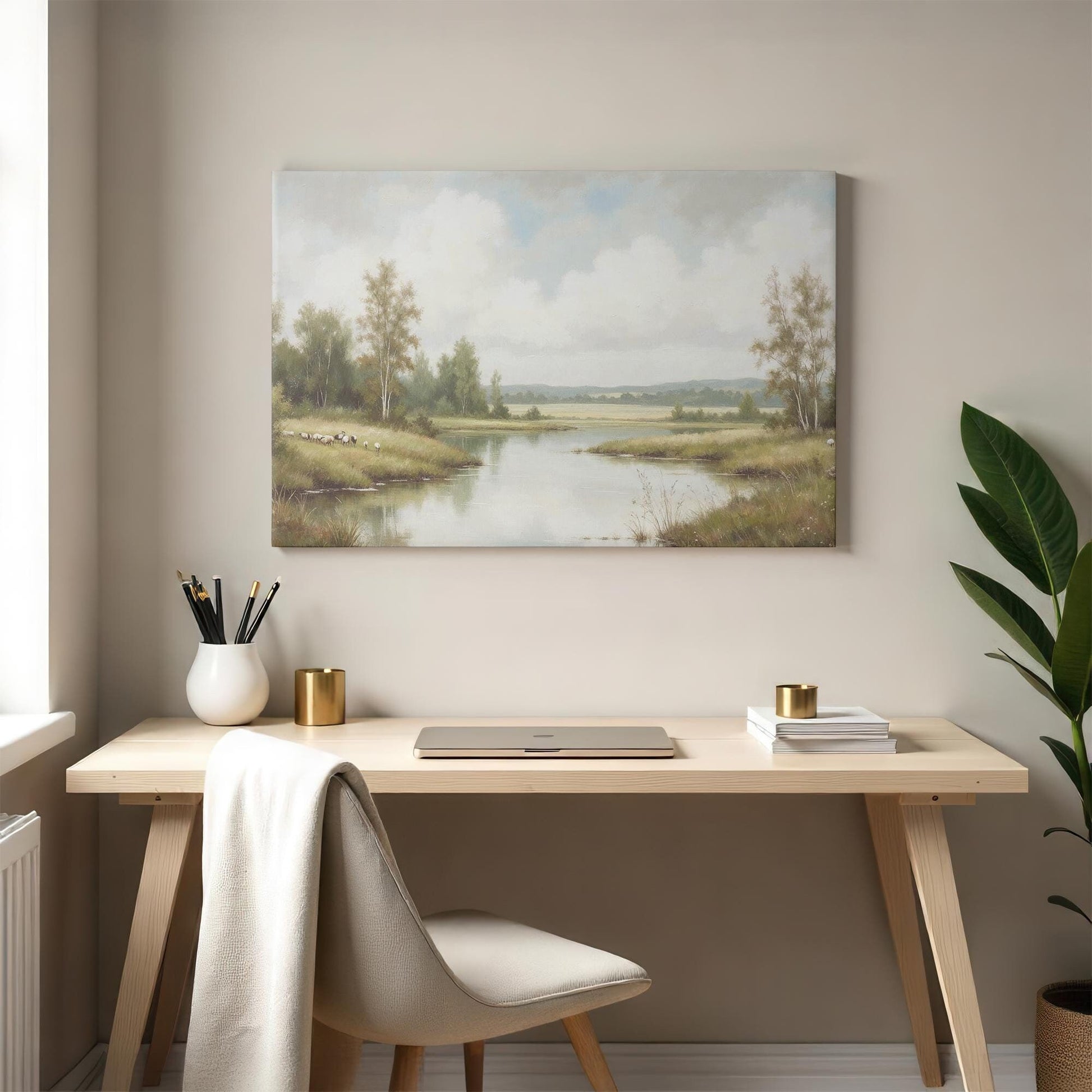 A serene landscape canvas print featuring a peaceful river and lush greenery hangs above a minimalist wooden desk. A beige chair, neutral decor, and a small potted plant create a tranquil workspace with natural tones.