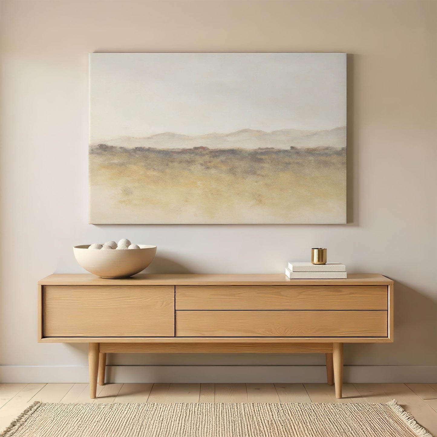 A modern sideboard with a minimalist canvas above it, displaying a soft, abstract landscape in neutral tones. A bowl of decorative stones and stacked books complement the clean, earthy aesthetic.