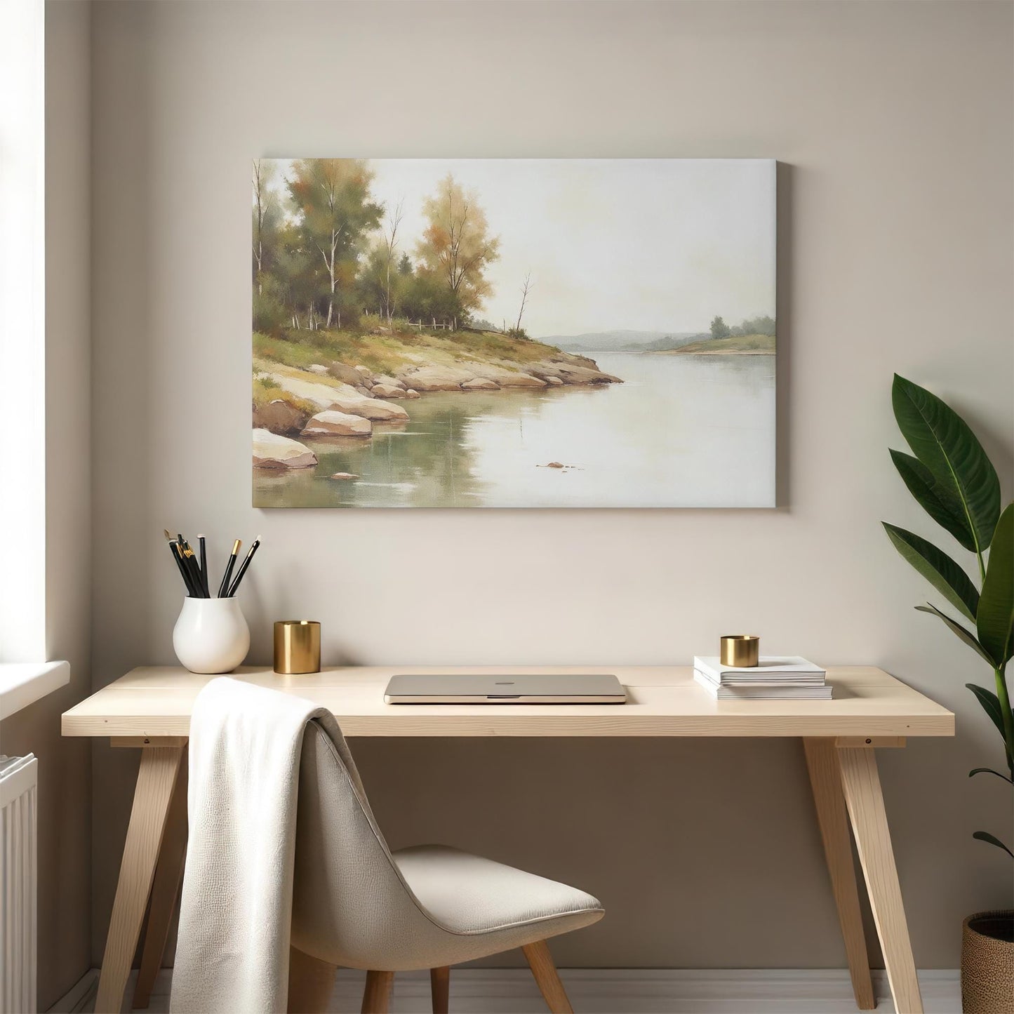 A calm and inviting workspace with a nature-inspired canvas print of a gentle river scene hanging above a wooden desk. A beige upholstered chair, gold-accented decor, and a green potted plant complete the neutral and modern aesthetic.
