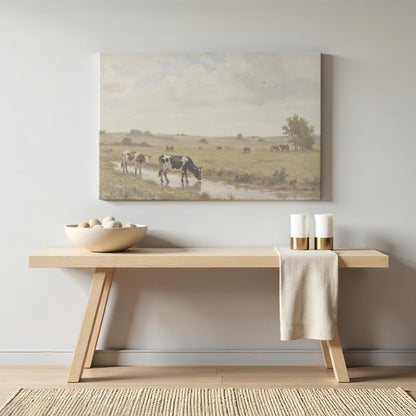A soft-toned pastoral cow painting displayed above a light wood bench with minimal decor, featuring neutral candles and a ceramic bowl with stones. A cozy, rustic home accent.