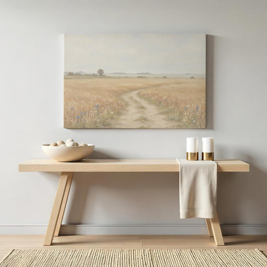 Neutral console table with a minimalist aesthetic, featuring a large canvas print of a golden wheat field with a winding dirt path. Styled with a ceramic bowl filled with smooth stones and modern gold-accented candles.