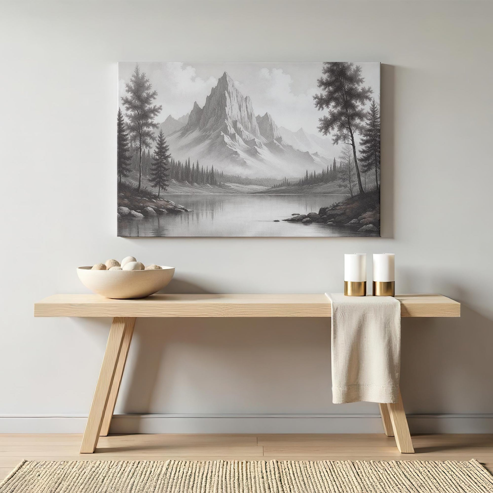 Monochrome mountain lake wall art styled above a sleek wooden console table with neutral decor, including candles and a woven bowl, creating a cozy yet modern rustic aesthetic in a contemporary living space.
