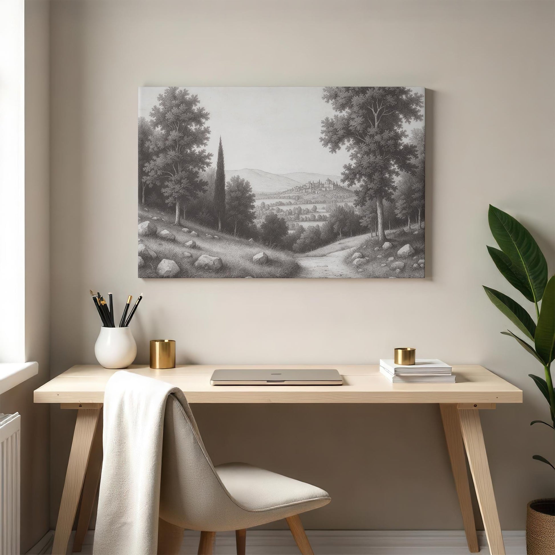 Elegant home office with a black and white countryside art piece above a modern desk, accented with a neutral chair, gold decor, and a potted plant.