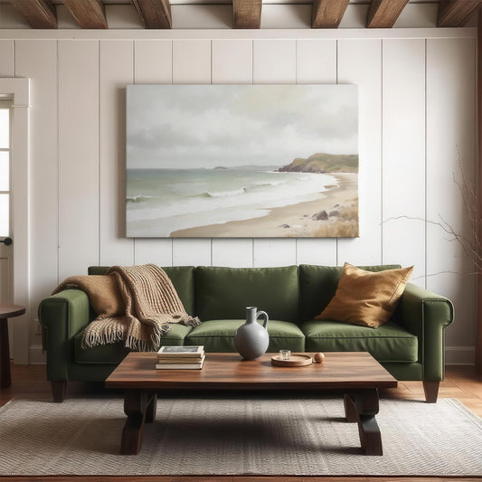 Coastal wall art above green sofa in cozy living room. Neutral decor with wood coffee table, beige throw, and soft lighting. Serene beach painting adds a calming coastal touch to modern farmhouse space.