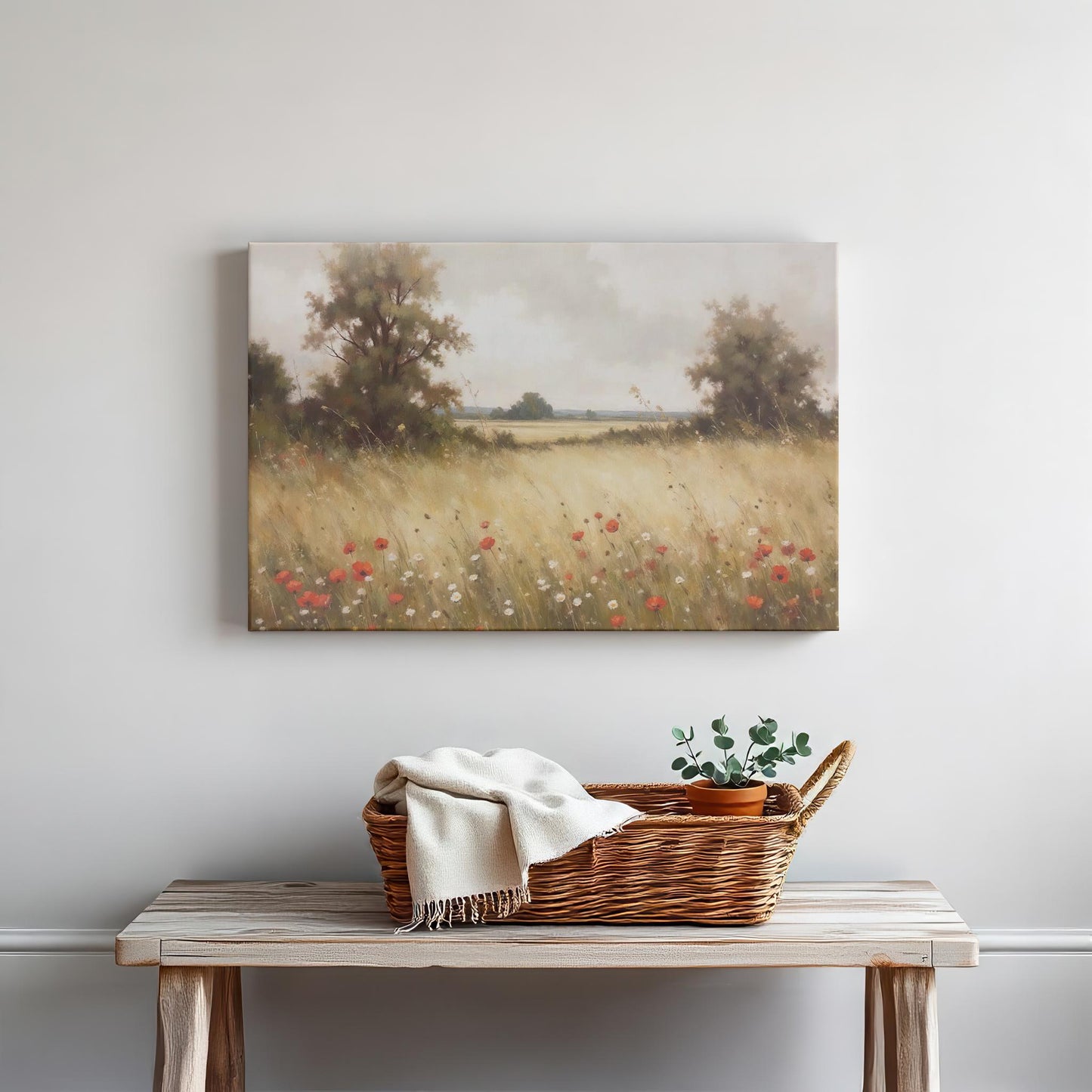 Rustic decor featuring a wooden table with a wicker basket, a white throw blanket, and a small potted plant. Above hangs a gallery-wrapped canvas titled &#39;Golden Meadow,&#39; depicting a serene field of wildflowers and poppies under a soft, cloudy sky.