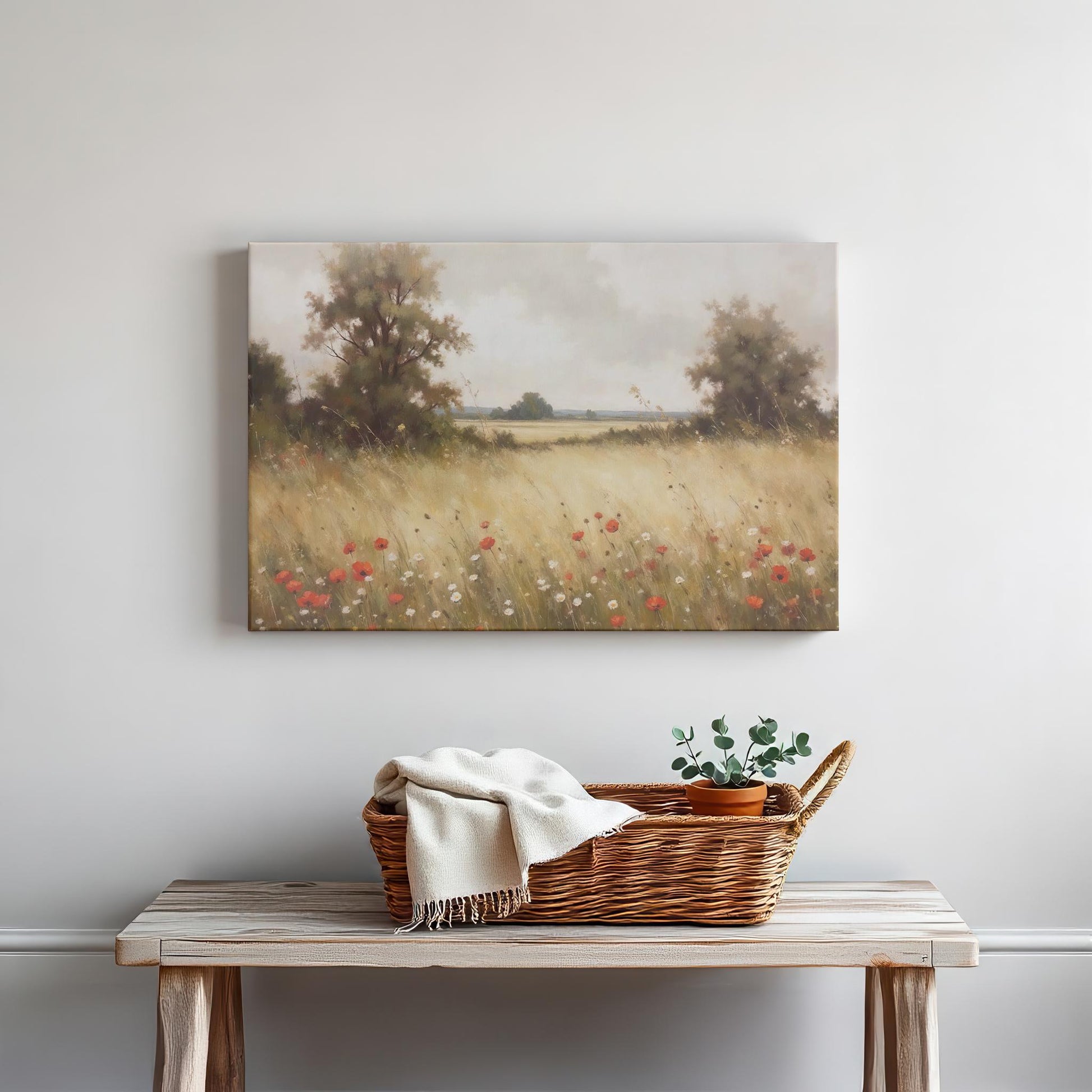 Rustic decor featuring a wooden table with a wicker basket, a white throw blanket, and a small potted plant. Above hangs a gallery-wrapped canvas titled &#39;Golden Meadow,&#39; depicting a serene field of wildflowers and poppies under a soft, cloudy sky.