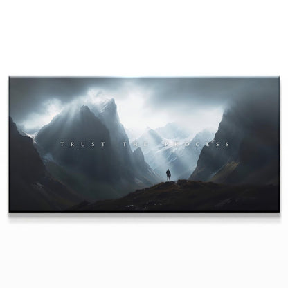 A majestic mountainous landscape with a figure standing in the distance beneath dramatic clouds. The text &quot;TRUST THE PROCESS&quot; is centered in a minimalist white font, creating an inspiring and bold contrast with the dark, moody sky.