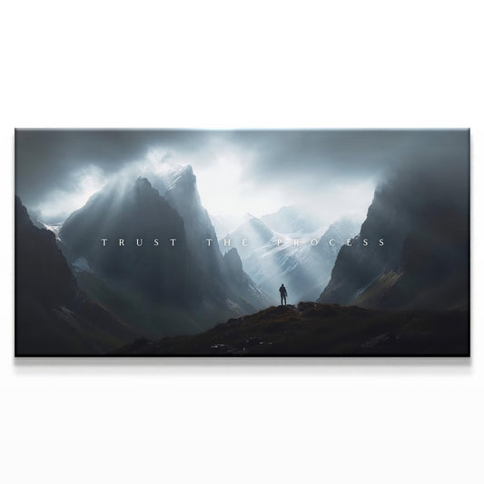 A majestic mountainous landscape with a figure standing in the distance beneath dramatic clouds. The text &quot;TRUST THE PROCESS&quot; is centered in a minimalist white font, creating an inspiring and bold contrast with the dark, moody sky.
