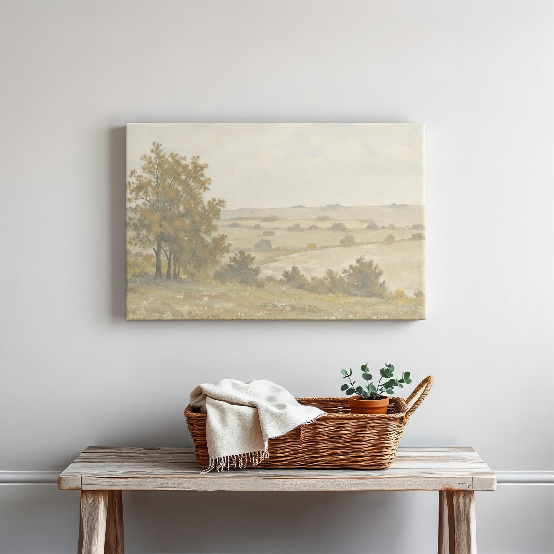 A tranquil countryside scene printed on canvas, hanging above a rustic wooden bench. A woven basket with a cozy blanket and a potted plant add a touch of organic warmth to the space, enhancing the painting&#39;s natural beauty.