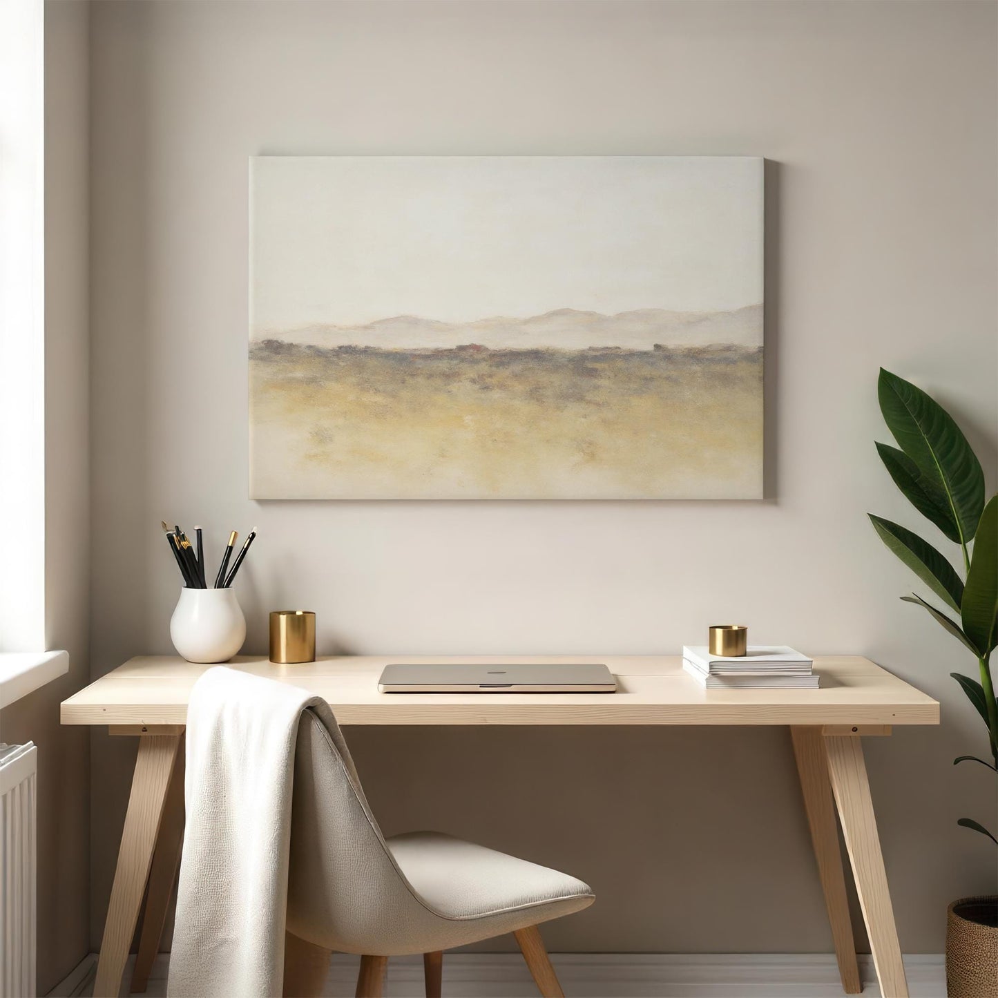 A cozy workspace with a light wood desk and a minimalist canvas featuring an abstract landscape in earthy tones. A laptop, books, and a green plant add to the serene, inspiring ambiance.