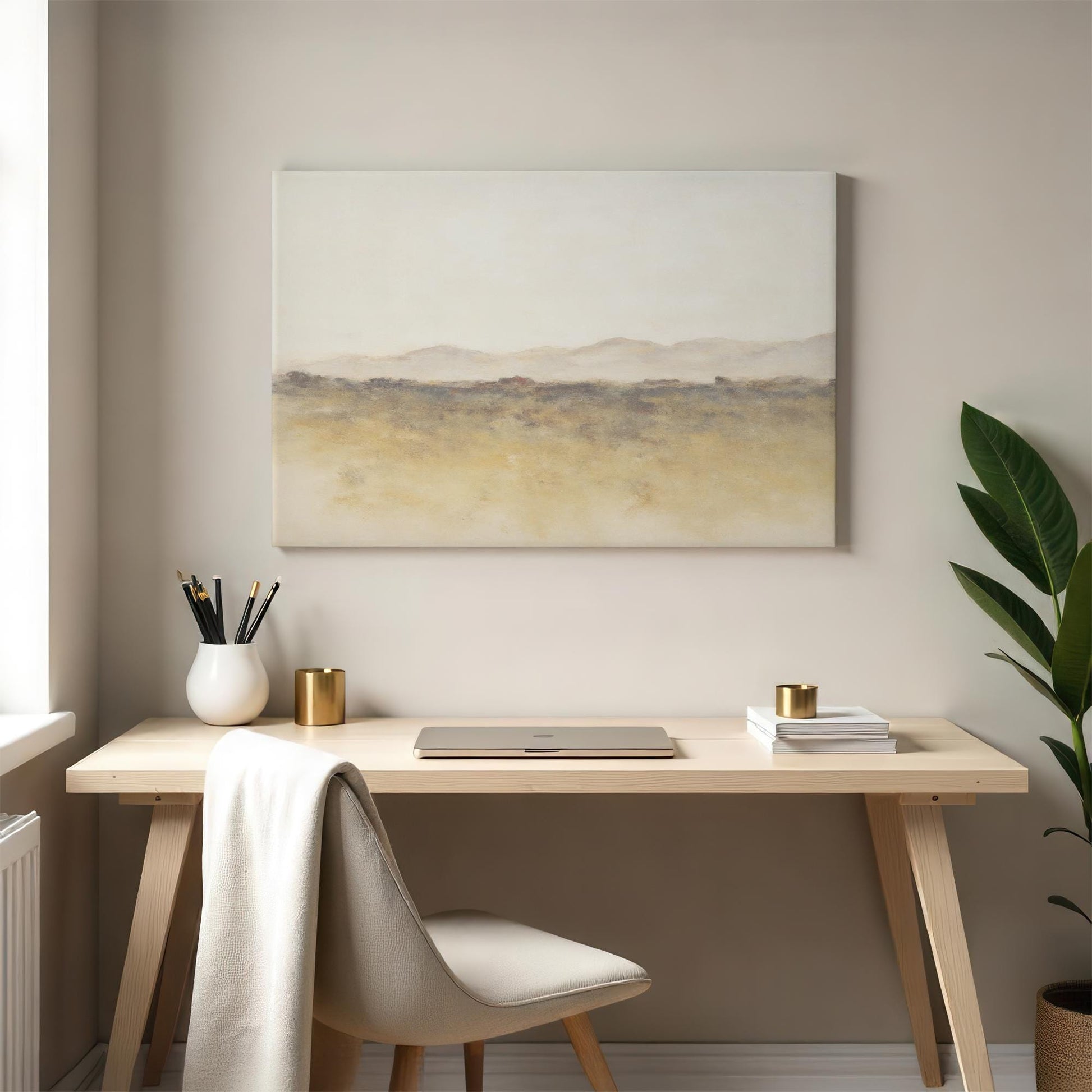 A cozy workspace with a light wood desk and a minimalist canvas featuring an abstract landscape in earthy tones. A laptop, books, and a green plant add to the serene, inspiring ambiance.
