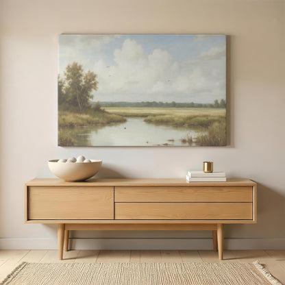 A rustic-inspired living space featuring a framed countryside landscape print above a mid-century modern wooden sideboard. Neutral tones, stacked books, and a ceramic bowl complement the soft hues of the artwork, creating a warm and inviting space.