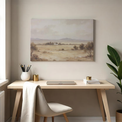 A neutral-hued canvas print of a tranquil desert landscape with rolling hills and a small house, complementing a modern home office space with a wooden desk, gold accents, and soft natural lighting.