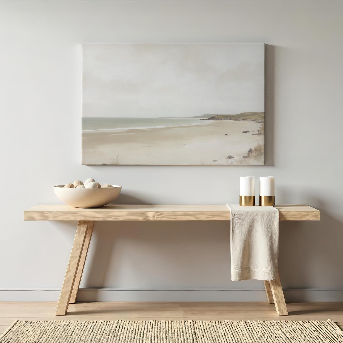 Neutral coastal artwork of a serene beach scene in soft muted tones, styled above a minimalist wooden console table. The decor features a modern, organic aesthetic with ceramic accents and gold candle holders.
