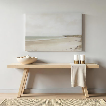 Neutral coastal artwork of a serene beach scene in soft muted tones, styled above a minimalist wooden console table. The decor features a modern, organic aesthetic with ceramic accents and gold candle holders.