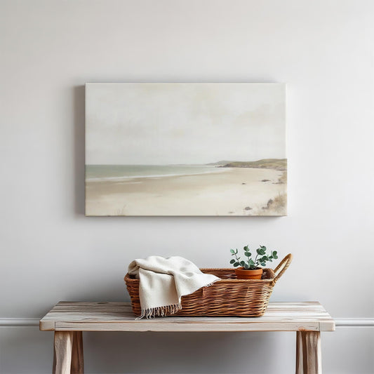Minimalist coastal wall art featuring a serene seascape canvas with soft neutral tones. Displayed above a wooden console table styled with a woven basket, a cozy throw, and a potted plant in a modern, coastal-inspired home.