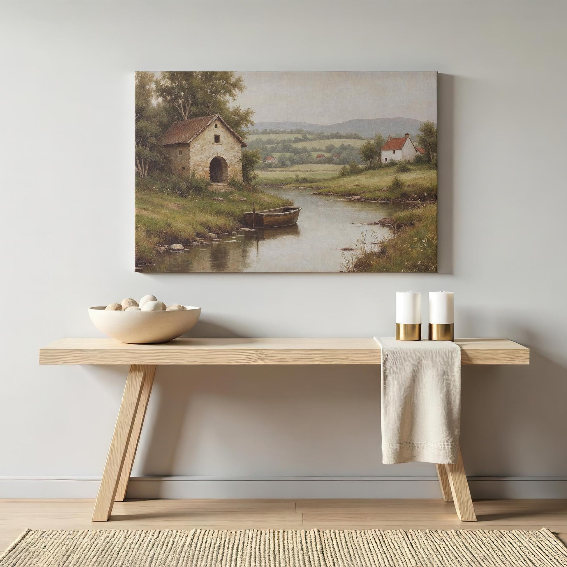 Traditional countryside canvas print featuring a peaceful river and rustic buildings, elegantly displayed above a wooden console with neutral decor. A timeless addition to vintage, cottagecore, or farmhouse interiors.