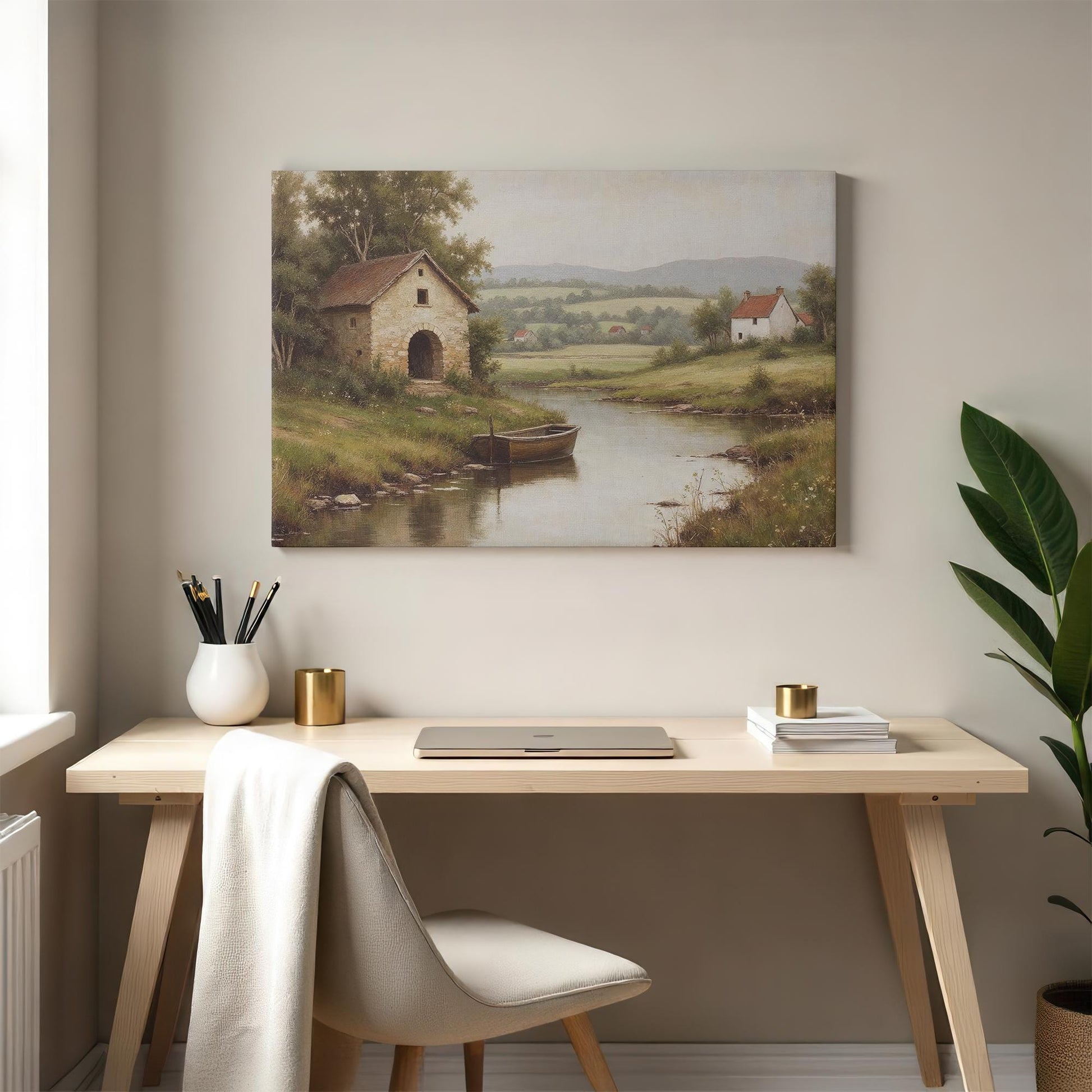 Countryside canvas wall art featuring a stone house, boat on a river, and rolling green hills, styled above a modern wooden desk with neutral decor and greenery. Ideal for office or home workspace aesthetics.