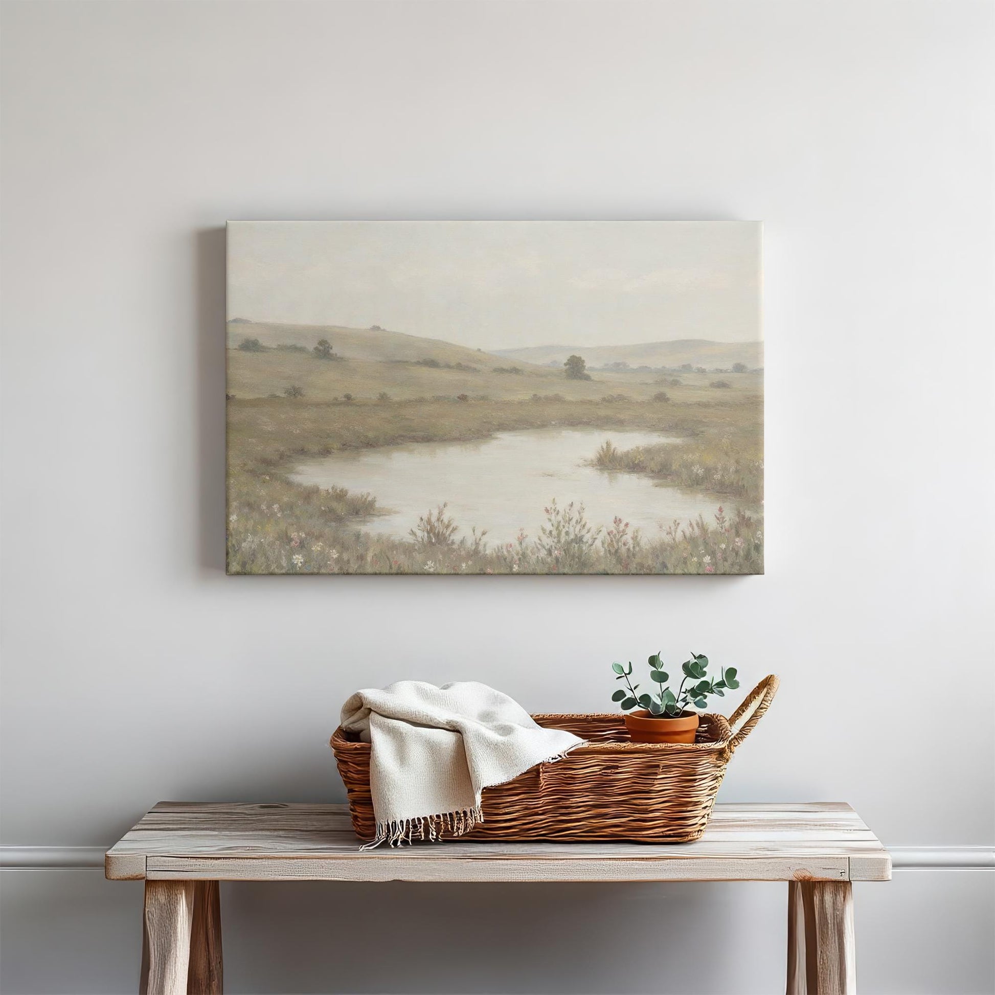 Tranquil landscape wall art above a rustic wooden bench with a woven basket, cozy throw, and potted plant. A peaceful countryside scene with soft earth tones, ideal for farmhouse or modern minimalist home decor.