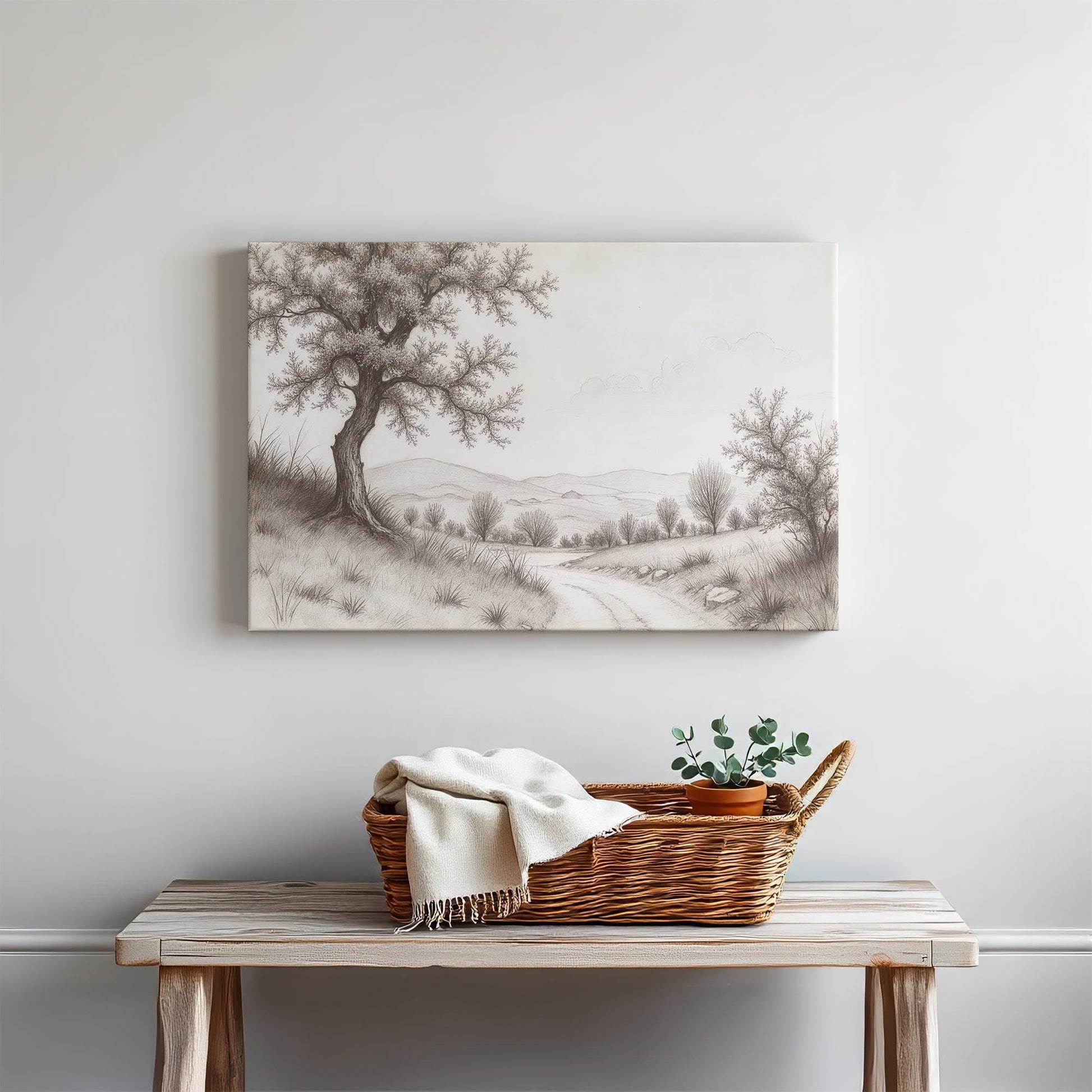 Rustic farmhouse-style entryway with a black and white tree landscape canvas wall art hanging above a wooden bench. Decor includes a woven basket, cozy blanket, and greenery.