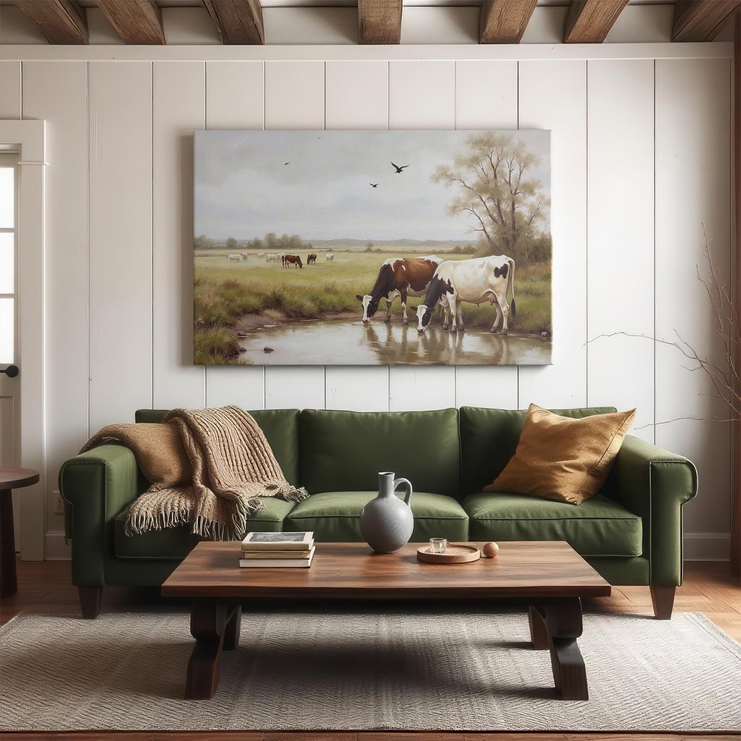 A cozy living room with a dark green sofa, a wooden coffee table, and a large wall art canvas depicting cows drinking by a pond. The neutral and earthy tones enhance the traditional farmhouse aesthetic.