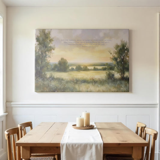 Bright dining room with a wooden table, chairs, and soft natural lighting. Above the table, a large canvas of Psalm 143:8 featuring a gentle sunrise over fields and trees creates an uplifting and serene ambiance.