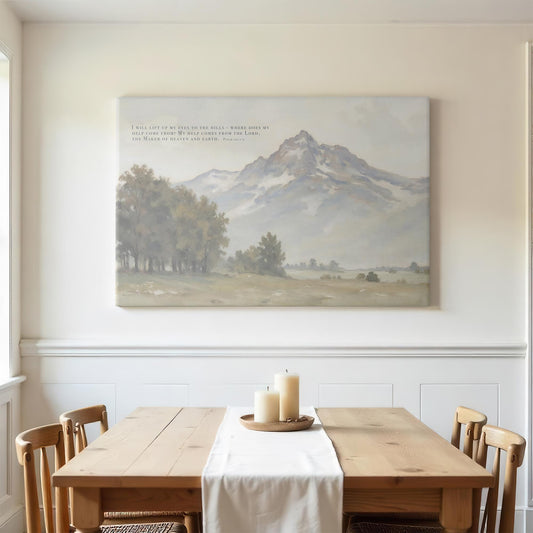 Simple dining room with wooden chairs and a light-colored table. A large canvas featuring Psalm 121:1-2 with a mountain landscape hangs on the wall, complementing the peaceful and minimalistic design of the space.