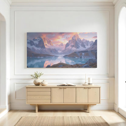 A large panoramic mountain wall art piece displayed in a modern living room with dark interior tones. The artwork showcases snow-capped peaks under a pink and orange sunset sky, their reflection shimmering in the still waters of an alpine lake. The dramatic light and shadow bring a sense of depth and awe, creating a luxurious and inspiring ambiance for any space designed for relaxation and contemplation.