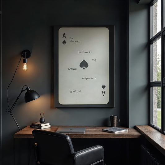 A moody, high-end office with a black leather chair, rustic wood desk, and a large Ace of Spades wall art. The dim lighting from a vintage Edison bulb lamp and soft window light creates an intimate, focused atmosphere. The artwork’s bold message reinforces a motivational, disciplined mindset, perfect for entrepreneurs and professionals.
