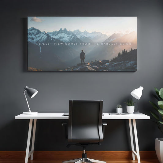 A modern minimalist office with a black and white desk setup featuring a large motivational mountain canvas print. The artwork depicts a hiker at sunrise with the quote &quot;The best view comes from the hardest climb&quot;, symbolizing success and determination. Clean white decor, desk lamps, and potted plants add contrast against the dark accent wall, making this workspace both stylish and inspiring.
